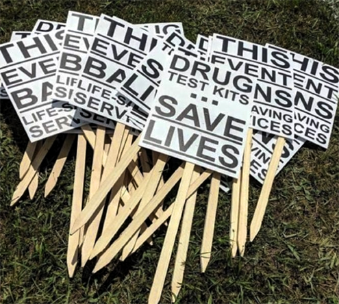 A pile of protest posters reading "Drug Test Kits Save Lives."