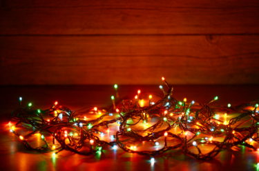 A string of Christmas lights tangled on the floor, lit up in a dark setting.